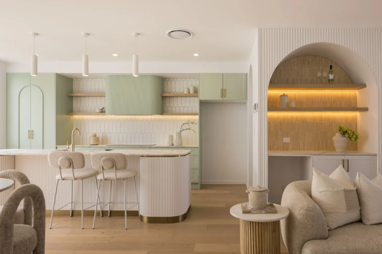 Open-plan kitchen with mint cabinets, ribbed island base, and arched alcove shelves with warm lighting.